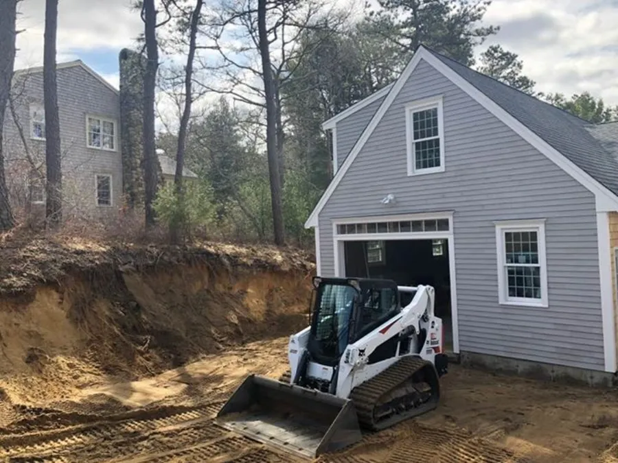 Skid steer grading beside a new garage